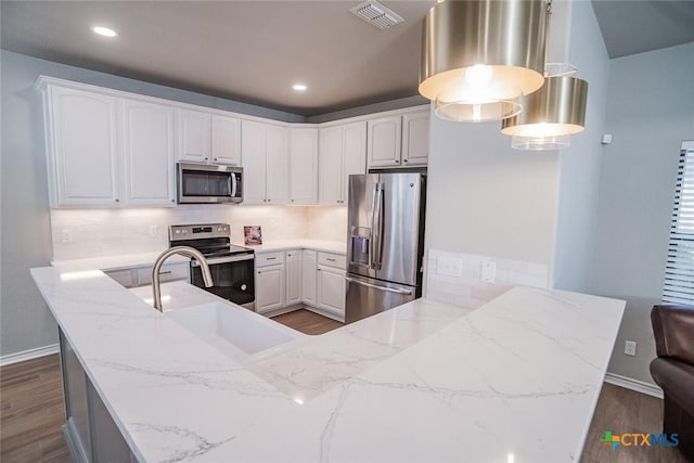 kitchen featuring visible vents, a sink, appliances with stainless steel finishes, a peninsula, and dark wood-style flooring