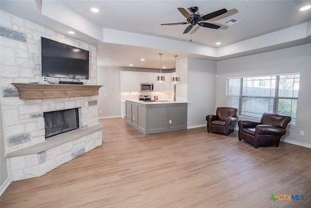 living area with visible vents, light wood-style flooring, baseboards, a stone fireplace, and a raised ceiling