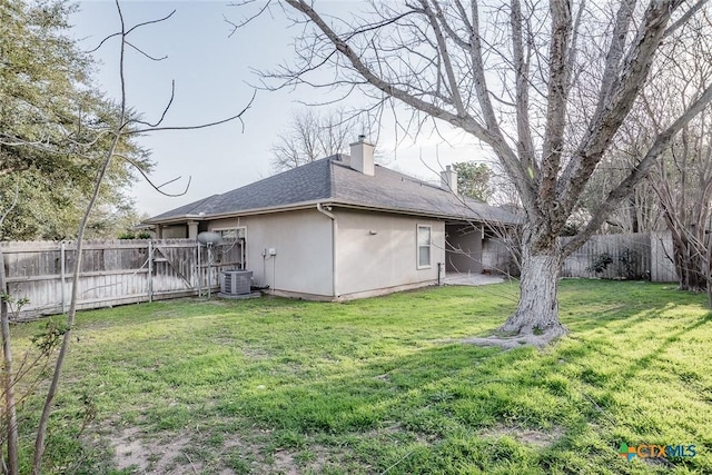 rear view of property with cooling unit, roof with shingles, a yard, a fenced backyard, and a chimney