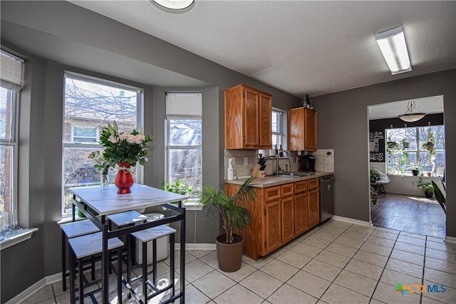 kitchen with light countertops, stainless steel dishwasher, a sink, and brown cabinets