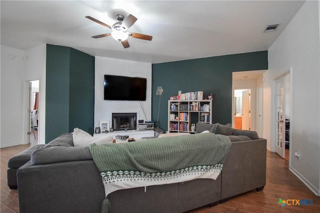 living room with ceiling fan, a large fireplace, wood finished floors, visible vents, and baseboards