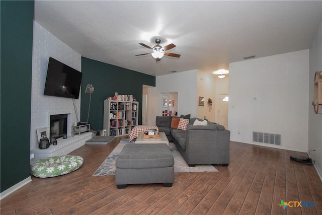 living room with ceiling fan, a fireplace, visible vents, and wood finished floors