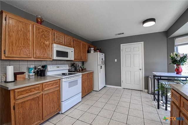 kitchen with brown cabinets, light countertops, visible vents, decorative backsplash, and white appliances