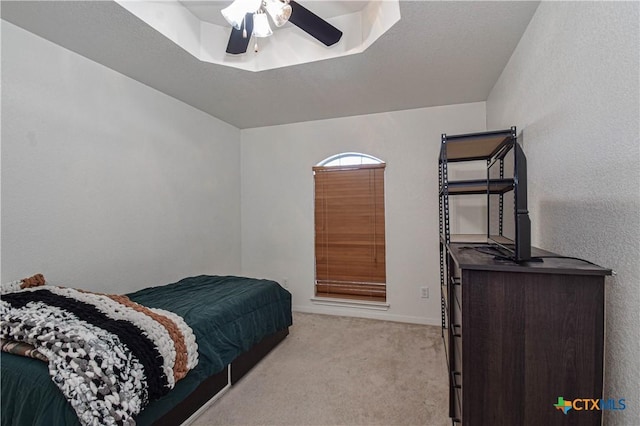 bedroom with light carpet, a textured wall, a tray ceiling, and a ceiling fan