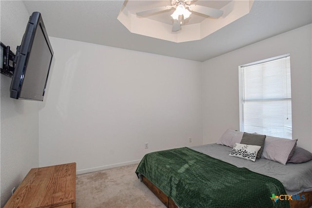 bedroom with light carpet, ceiling fan, a tray ceiling, and baseboards