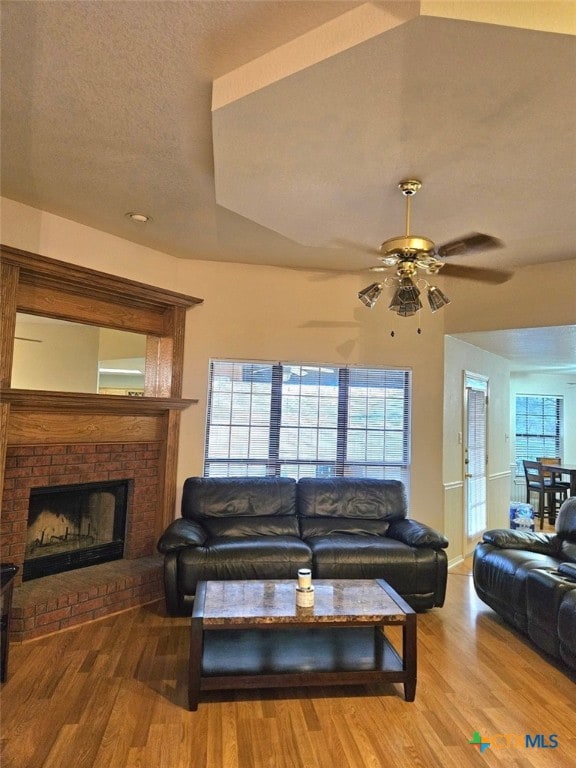 living room featuring hardwood / wood-style floors, a fireplace, a textured ceiling, and ceiling fan