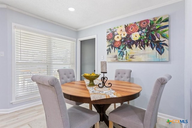 dining area with light wood finished floors, baseboards, ornamental molding, and a textured ceiling