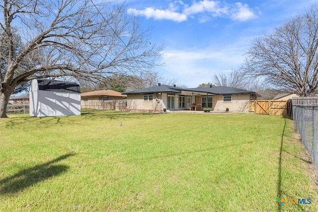 rear view of house with a lawn, a fenced backyard, a gate, a storage unit, and an outdoor structure