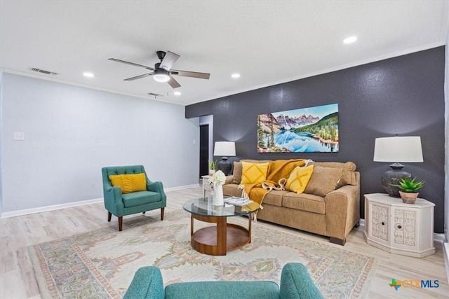 living area with an accent wall, wood finished floors, visible vents, and crown molding