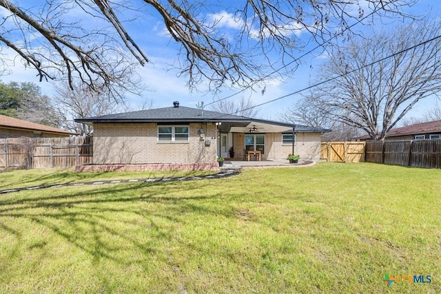 rear view of house with a fenced backyard, a patio, brick siding, and a lawn