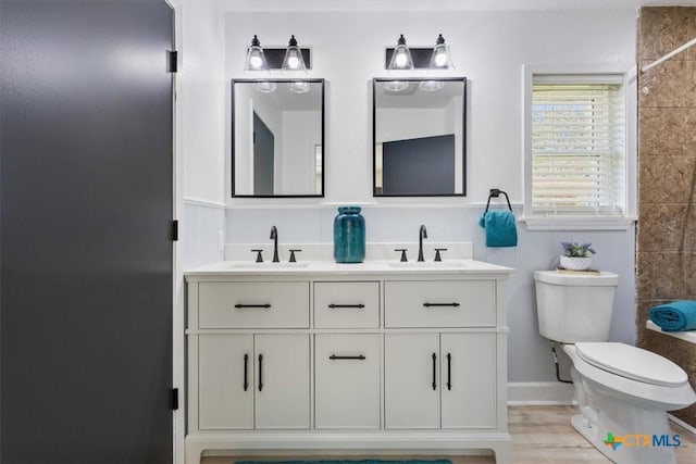 bathroom with toilet, double vanity, a sink, and wood finished floors