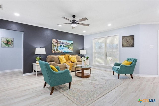 living area featuring baseboards, an accent wall, ornamental molding, and light wood-style floors