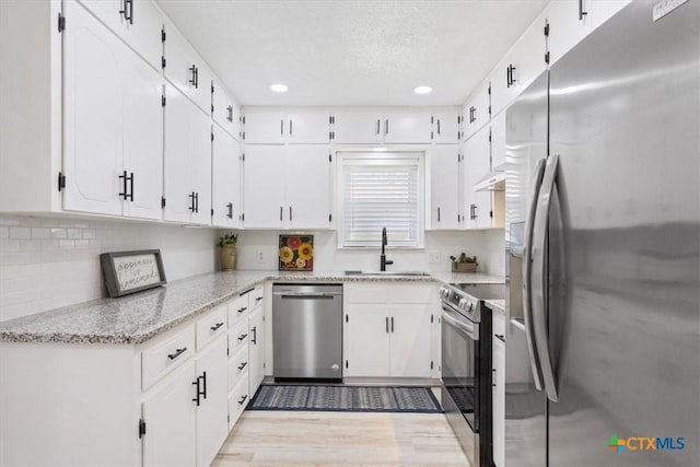 kitchen featuring stainless steel appliances, light wood-style flooring, white cabinetry, a sink, and light stone countertops