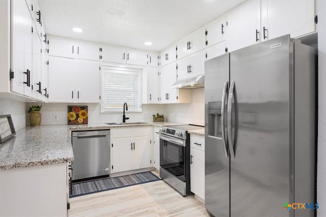 kitchen featuring light stone counters, under cabinet range hood, stainless steel appliances, a sink, and white cabinets