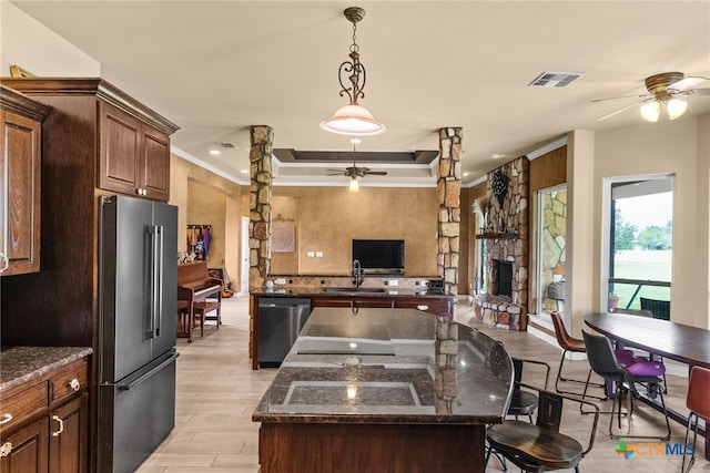 kitchen featuring a stone fireplace, appliances with stainless steel finishes, light hardwood / wood-style floors, dark stone countertops, and a center island