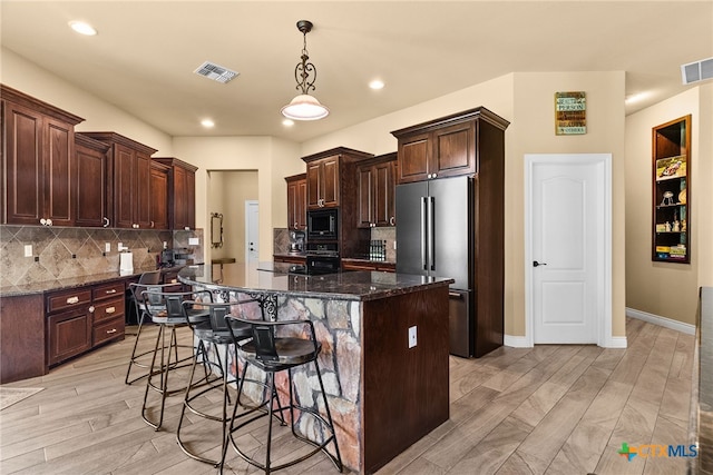 kitchen with black appliances, dark stone countertops, light hardwood / wood-style floors, and a breakfast bar