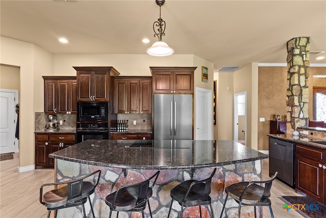 kitchen featuring black appliances, dark stone countertops, hanging light fixtures, light wood-type flooring, and decorative backsplash