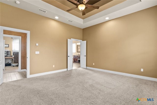 empty room with light colored carpet, ceiling fan, and a raised ceiling