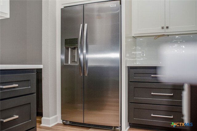 kitchen with white cabinetry, stainless steel refrigerator with ice dispenser, decorative backsplash, and light wood-type flooring