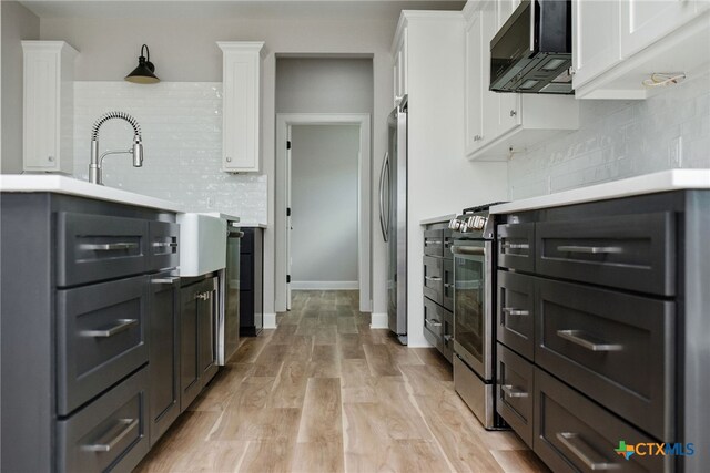 kitchen with white cabinets, light hardwood / wood-style flooring, stainless steel appliances, and backsplash