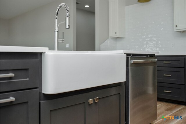 room details featuring backsplash, white cabinetry, sink, light hardwood / wood-style floors, and stainless steel dishwasher