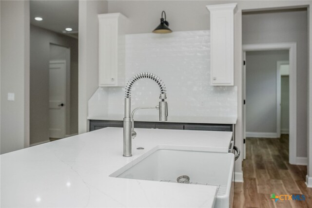 kitchen with backsplash, white cabinetry, sink, and hardwood / wood-style flooring