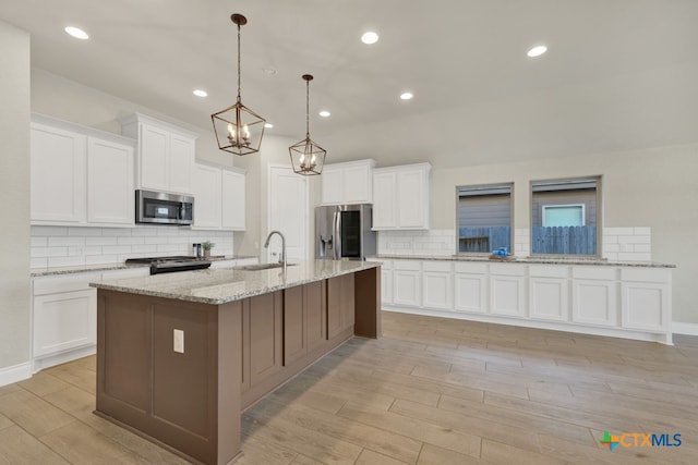 kitchen with stainless steel appliances, white cabinets, sink, light wood-type flooring, and decorative light fixtures