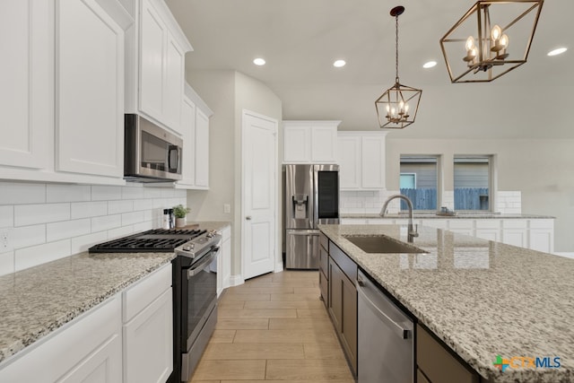 kitchen with stainless steel appliances, light stone counters, white cabinets, hanging light fixtures, and sink