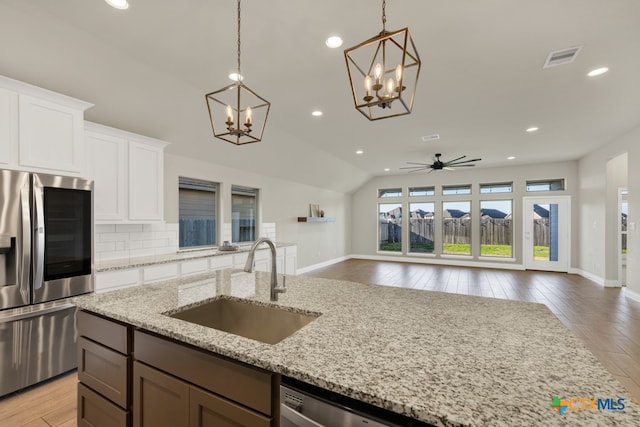 kitchen with stainless steel appliances, white cabinetry, sink, light stone counters, and lofted ceiling