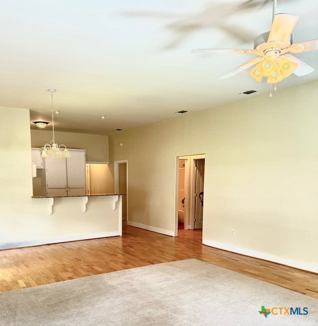 unfurnished room featuring ceiling fan with notable chandelier and light hardwood / wood-style floors