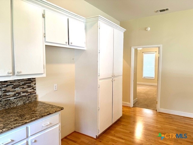 kitchen featuring white cabinetry, light hardwood / wood-style flooring, dark stone counters, and backsplash