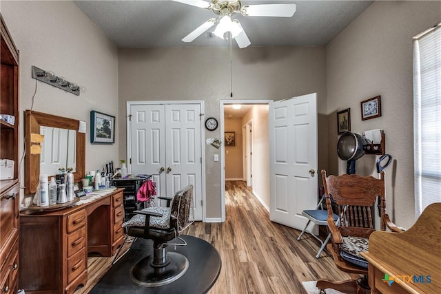 home office with hardwood / wood-style flooring, ceiling fan, a textured ceiling, and a towering ceiling