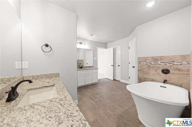 bathroom featuring a bathtub, vanity, hardwood / wood-style floors, and tile walls