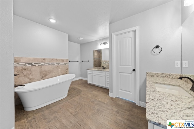 bathroom featuring hardwood / wood-style floors, a tub, vanity, and a textured ceiling