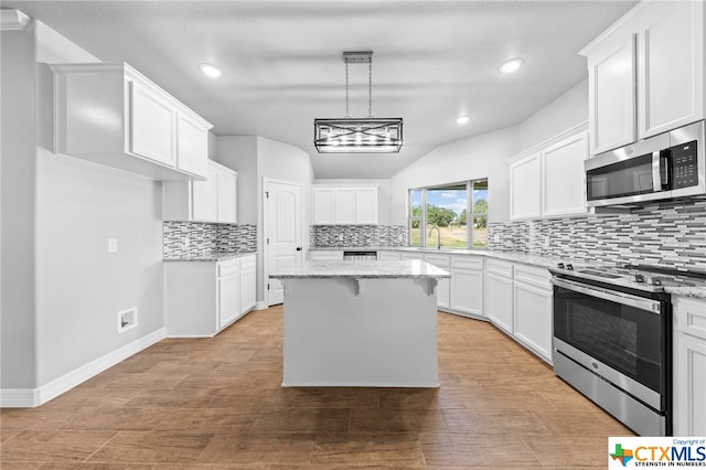 kitchen with white cabinets, light stone counters, appliances with stainless steel finishes, and a center island