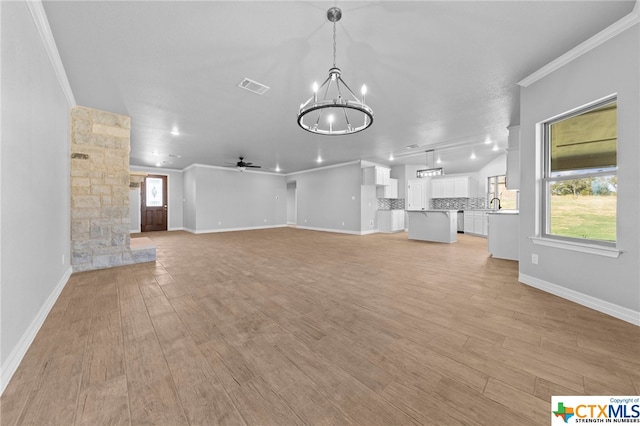 unfurnished living room with ceiling fan with notable chandelier, light hardwood / wood-style flooring, and ornamental molding