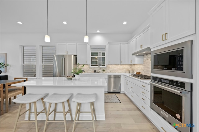 kitchen featuring a center island, appliances with stainless steel finishes, white cabinets, pendant lighting, and backsplash