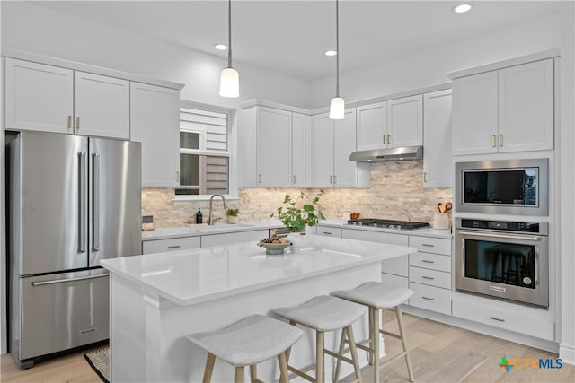 kitchen with a kitchen island, decorative light fixtures, white cabinetry, sink, and stainless steel appliances