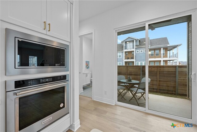 kitchen with built in microwave, stainless steel oven, white cabinetry, and light wood-type flooring