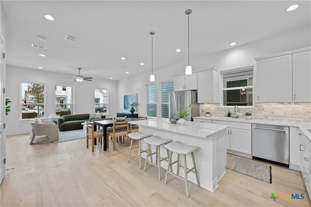 kitchen featuring a breakfast bar, hanging light fixtures, stainless steel appliances, a center island, and white cabinets