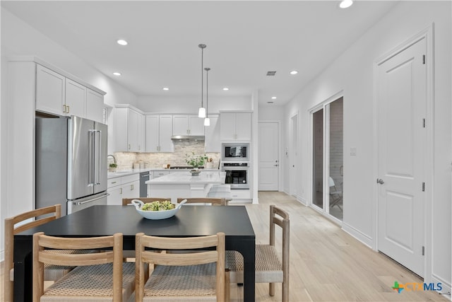 kitchen with appliances with stainless steel finishes, backsplash, white cabinets, a kitchen island, and decorative light fixtures