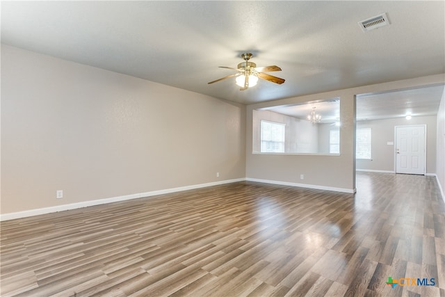 empty room with a textured ceiling, hardwood / wood-style floors, and ceiling fan with notable chandelier