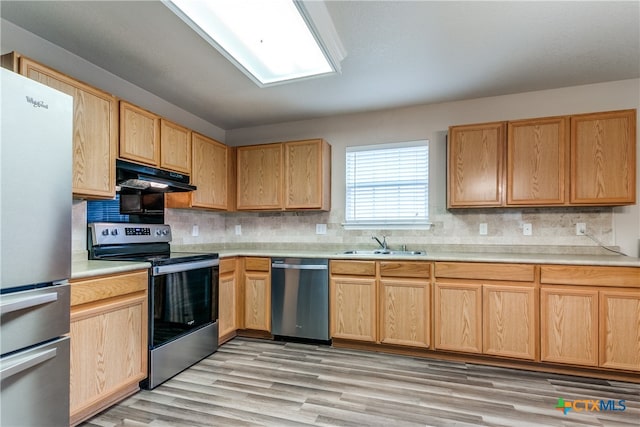 kitchen with tasteful backsplash, appliances with stainless steel finishes, sink, and light hardwood / wood-style floors