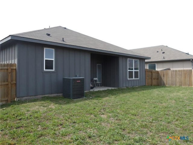 rear view of property featuring board and batten siding, a lawn, a fenced backyard, and central AC unit