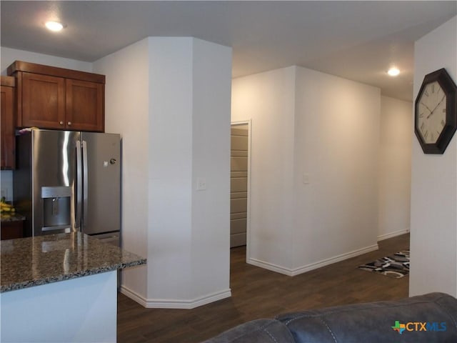 kitchen featuring dark stone counters, baseboards, brown cabinetry, stainless steel refrigerator with ice dispenser, and dark wood-type flooring