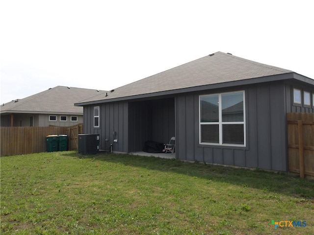 back of house with board and batten siding, a fenced backyard, a yard, and central AC