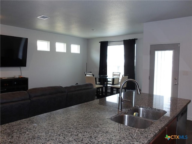 kitchen with open floor plan, stone counters, visible vents, and a sink