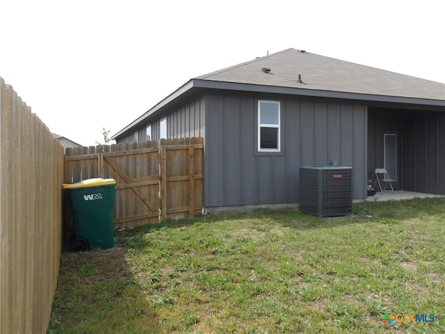 exterior space with board and batten siding, a lawn, central AC unit, and fence