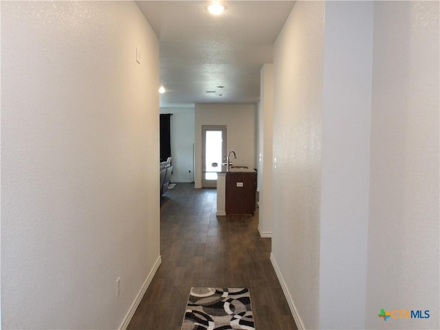 corridor featuring baseboards, a sink, and dark wood finished floors