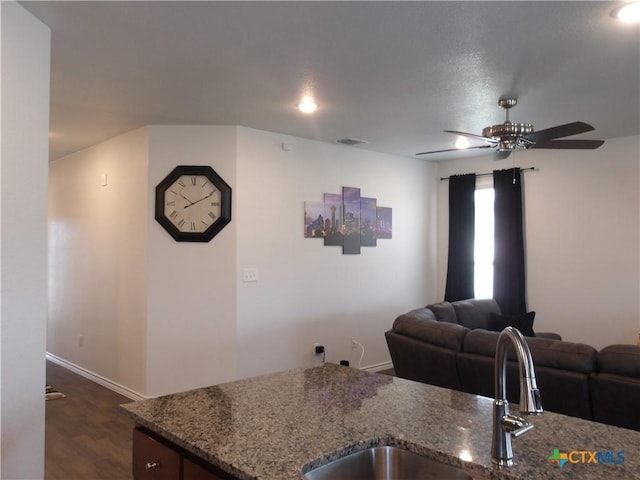 kitchen featuring a sink, dark wood finished floors, open floor plan, a ceiling fan, and stone countertops